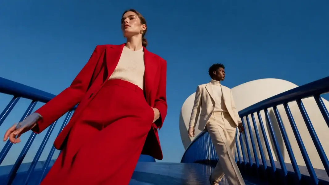 Two fashion models in red and cream suits walking through blue modern architecture
