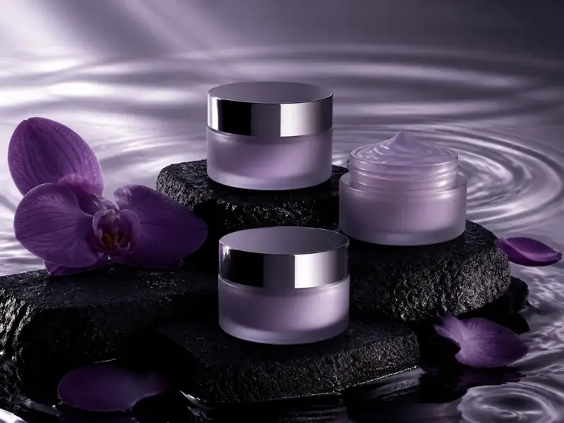 Lavender cosmetic jars arranged on black stones with orchids and rippling water