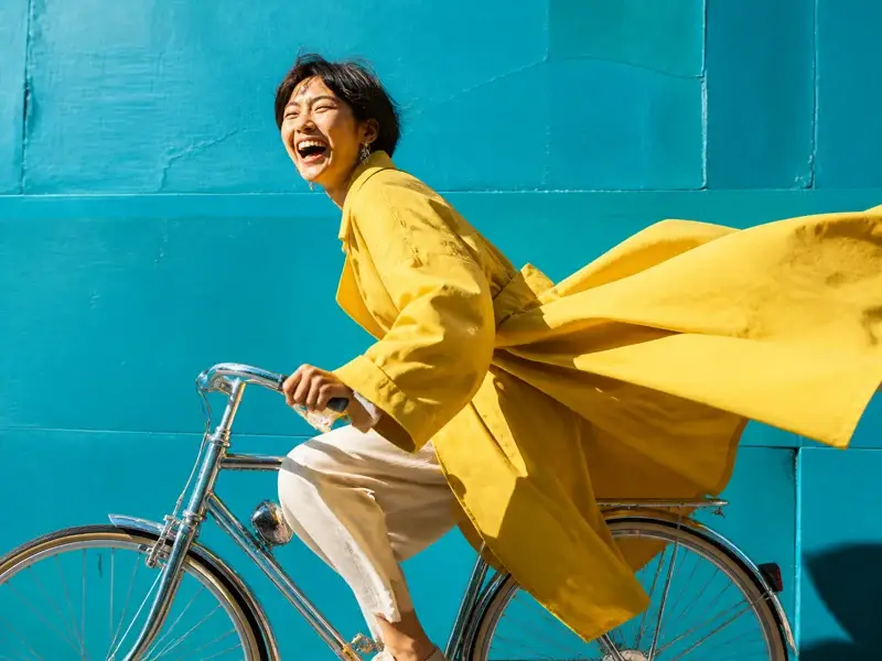 Smiling cyclist in a yellow coat riding past a turquoise wall