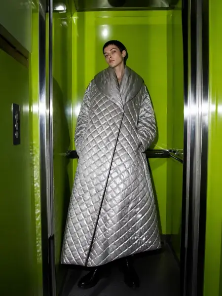 Fashion model in a silver quilted coat standing in a lime-green elevator